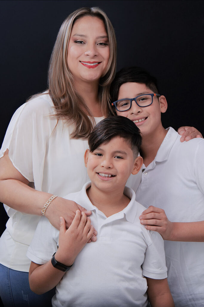 Madre con sus dos hijos en polos blancos, retrato familiar sobre fondo negro en estudio, Barranco
